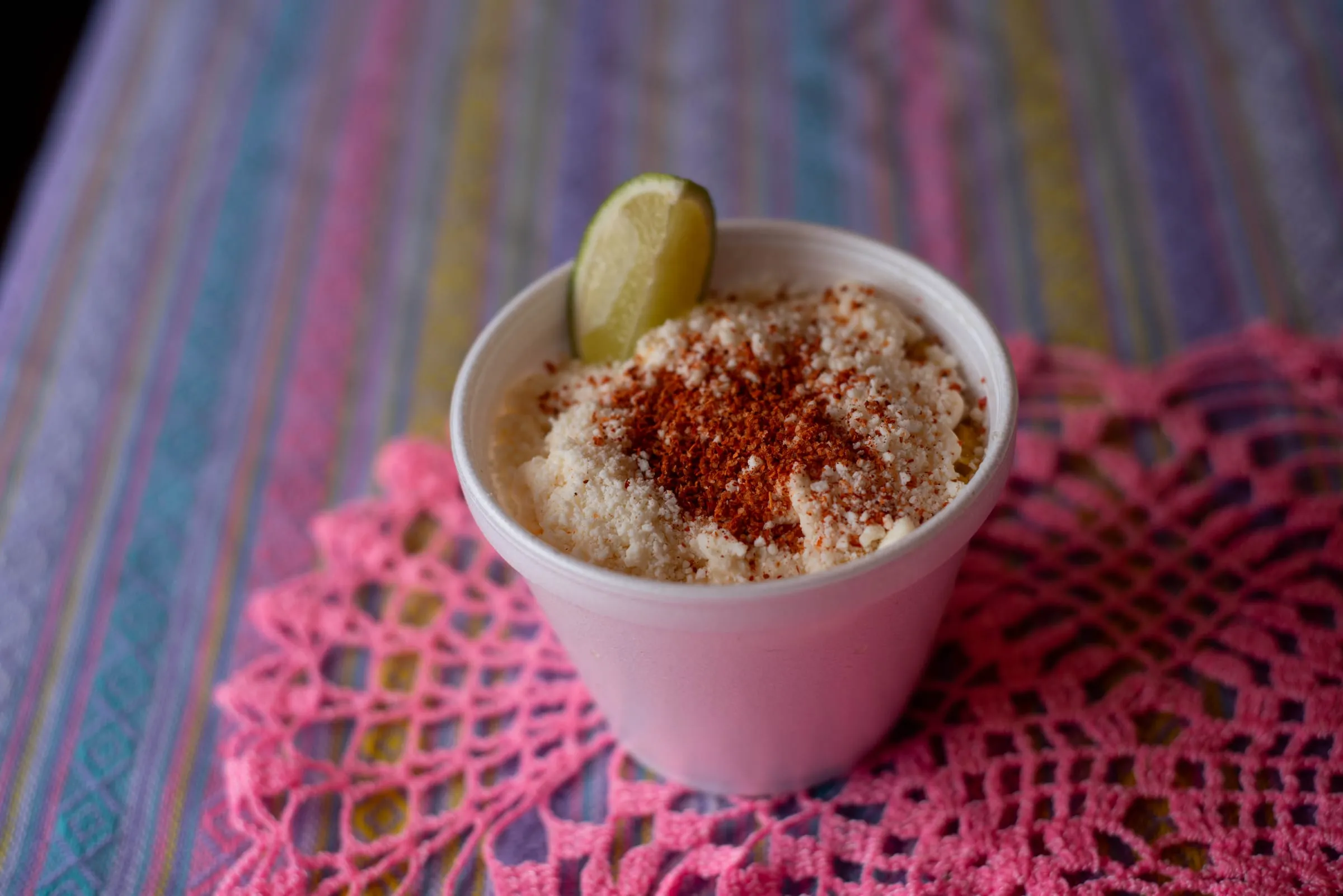 A cup of esquites topped with chile powder and a lime wedge