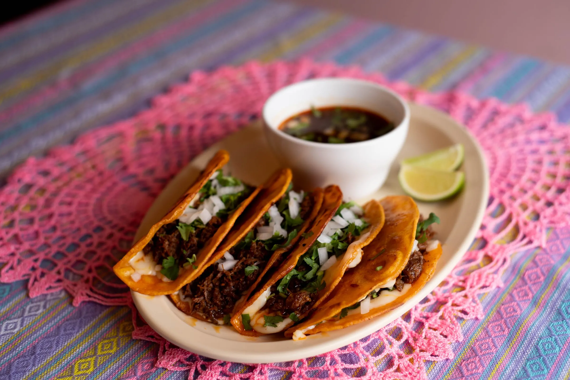 Quesabirria tacos on a plate with a cup of consomé and lime