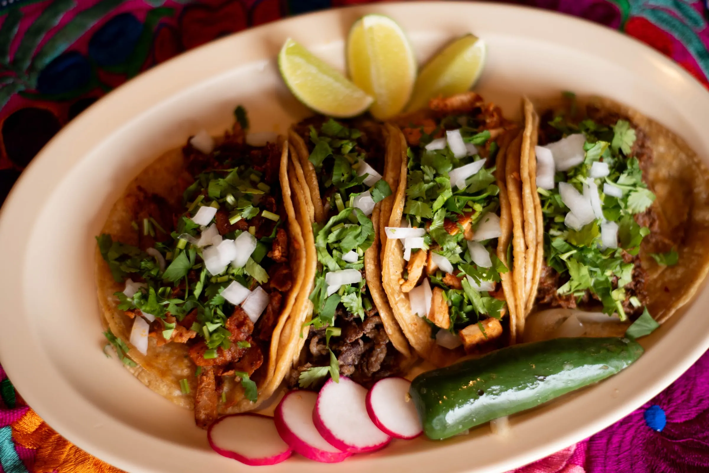 Three tacos topped with cilantro and onion, with lime, radish and a grilled pepper